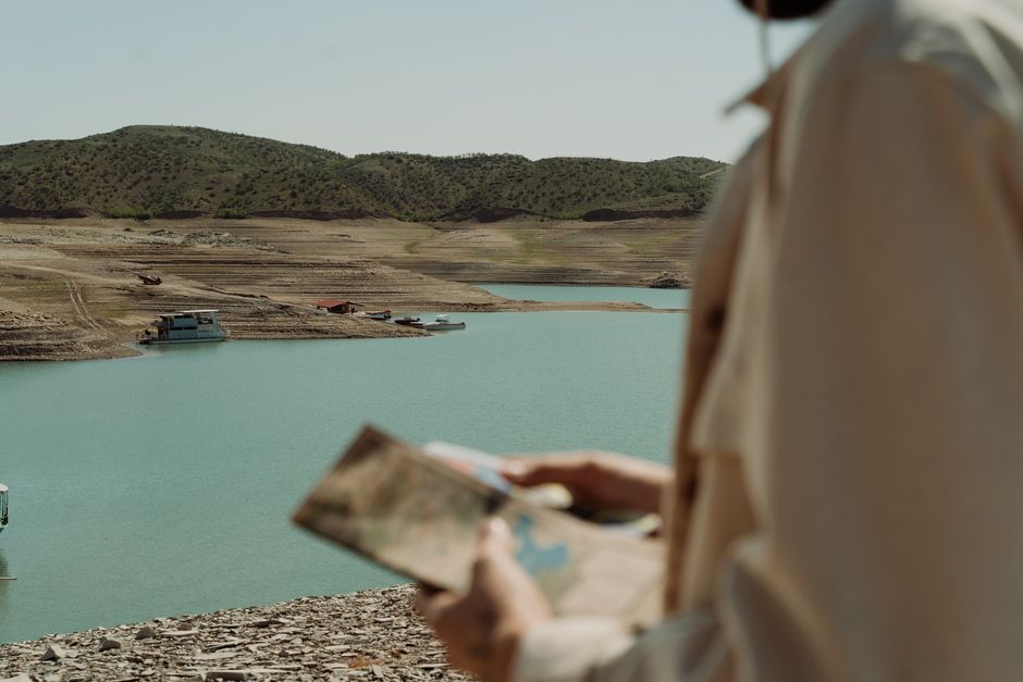 Traveler studies map by tranquil lake surrounded by hills.