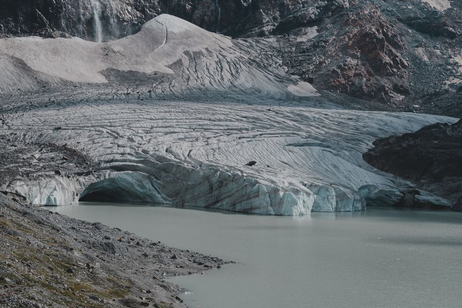 Majestic glacier with meltwater lake in a rugged mountain setting.